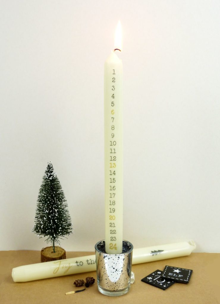 Adventskalenderkerze angezündet in Kerzenständer